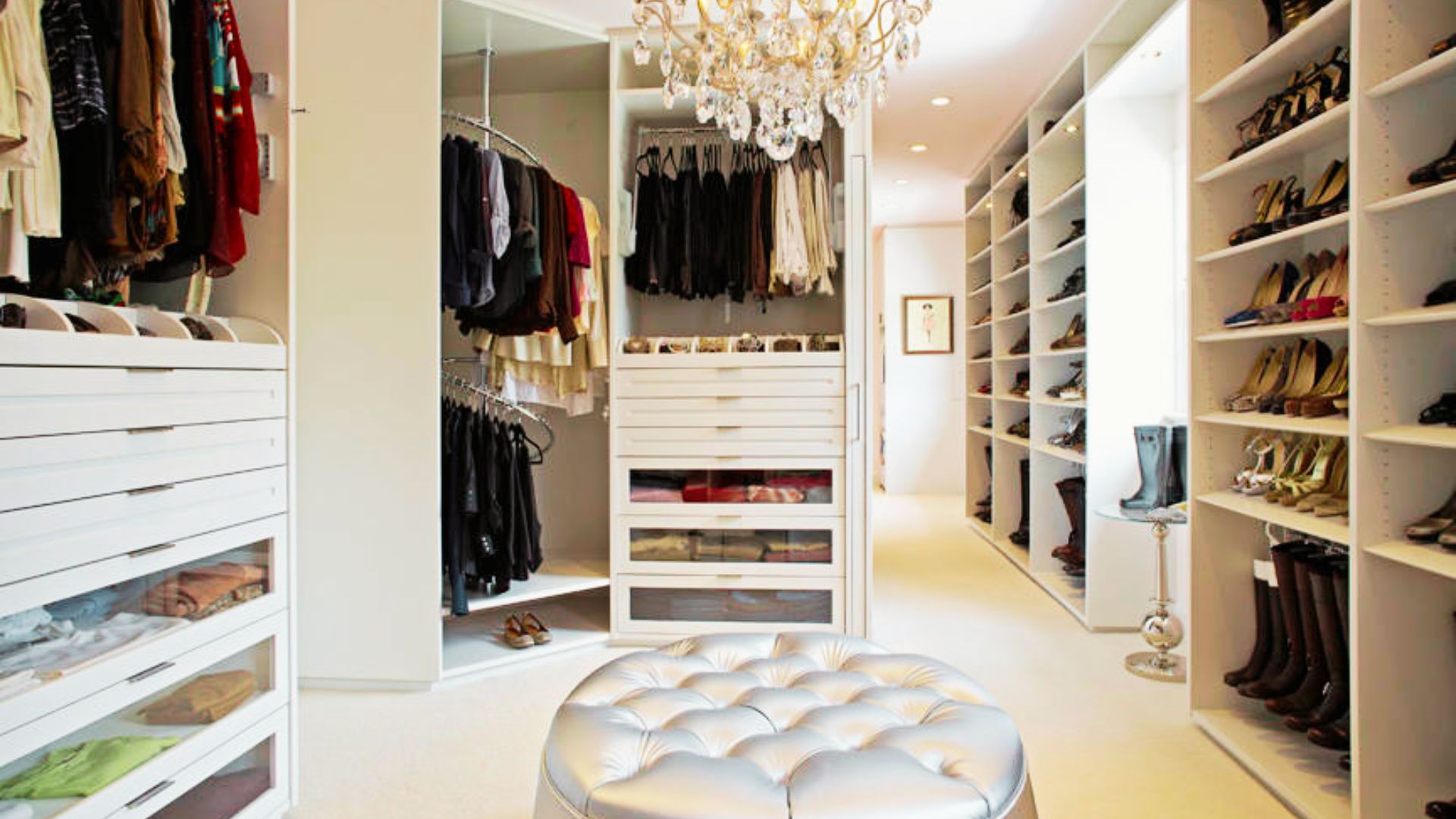 A sunlit luxury walk-in closet with marble island, built-in cabinetry, and floor-to-ceiling windows overlooking lush greenery.