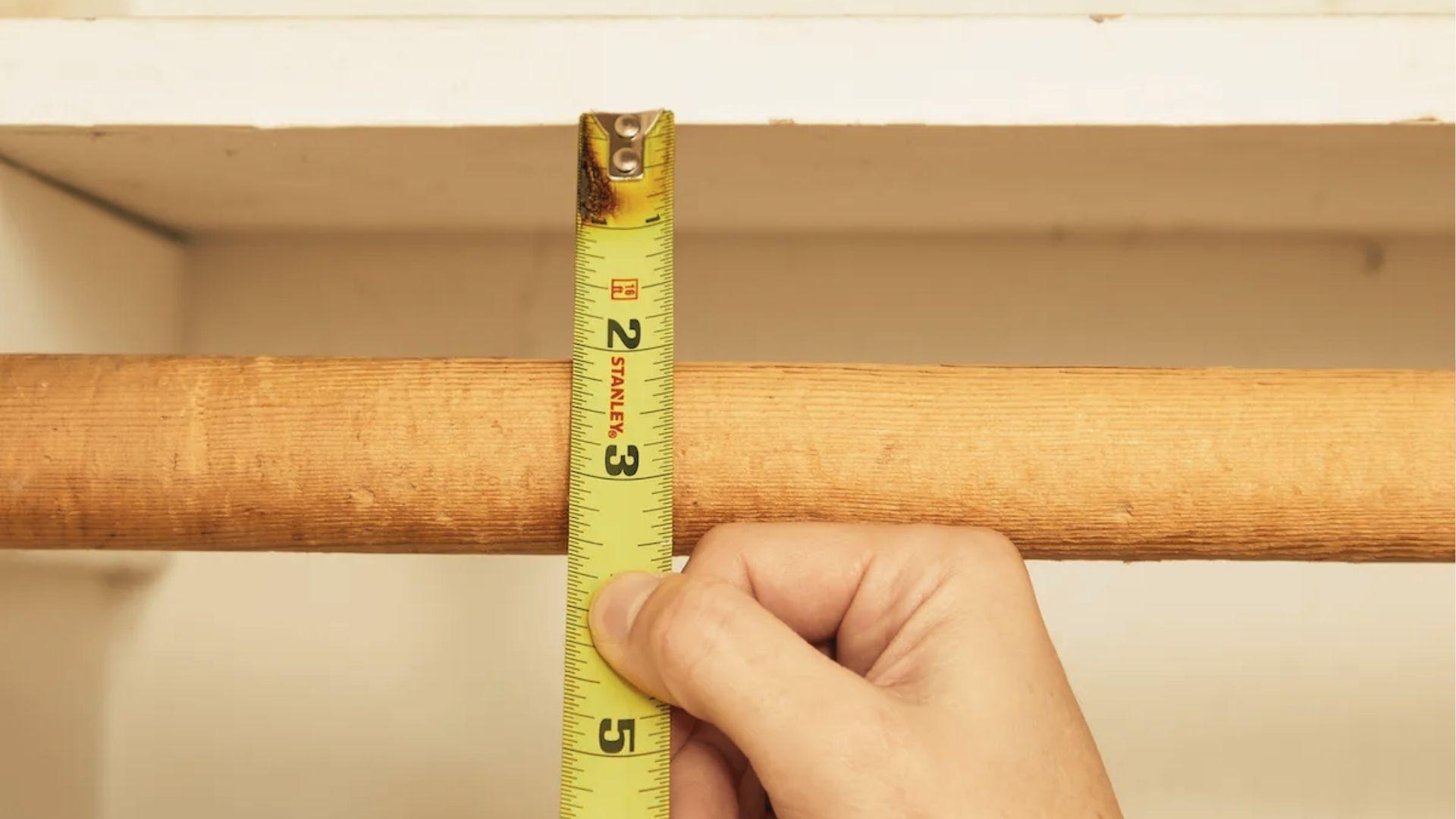 Close-up of a tape measure showing the vertical distance between a closet rod and the shelf above.