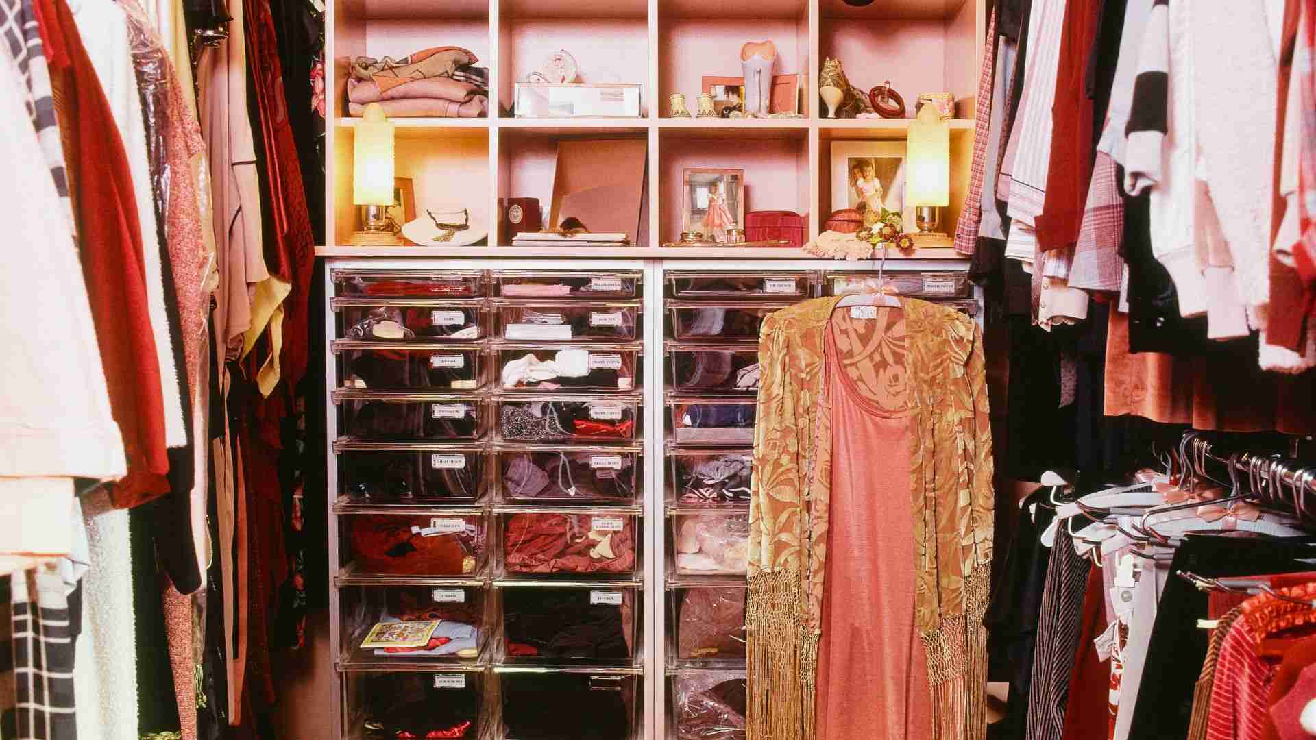 Warm-lit wardrobe with sliding glass doors, LED vanity mirror, hanging clothes, and storage units.