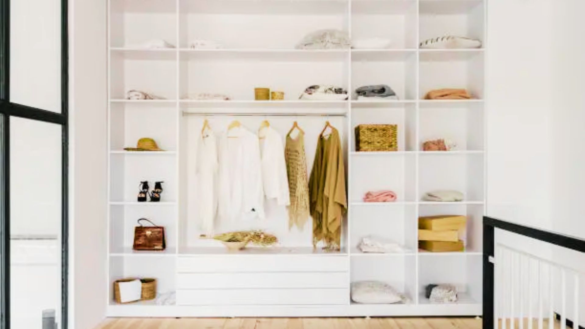 Minimalist white open wardrobe with cubbies, hanging garments, folded clothes, shoes, hats, and baskets.