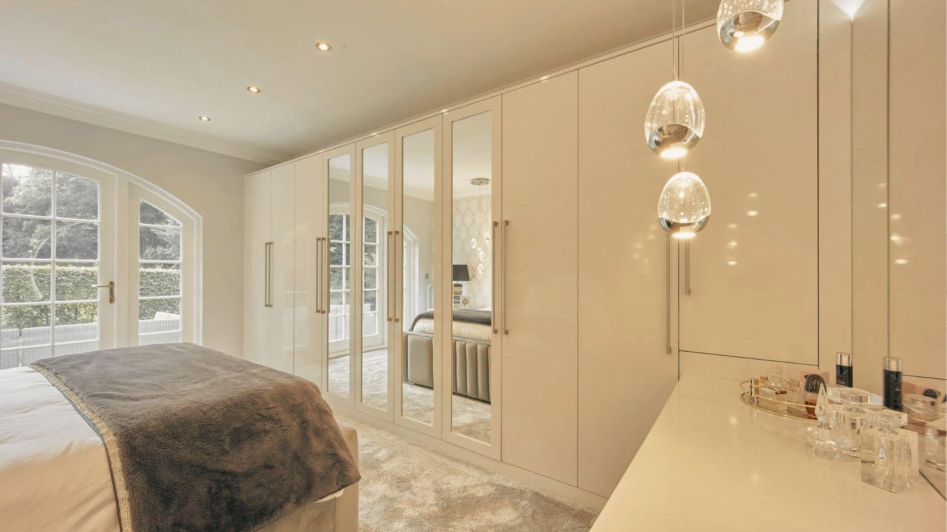Elegant white gloss wardrobe with tall hinged doors and mirrored center panels in a bright bedroom.