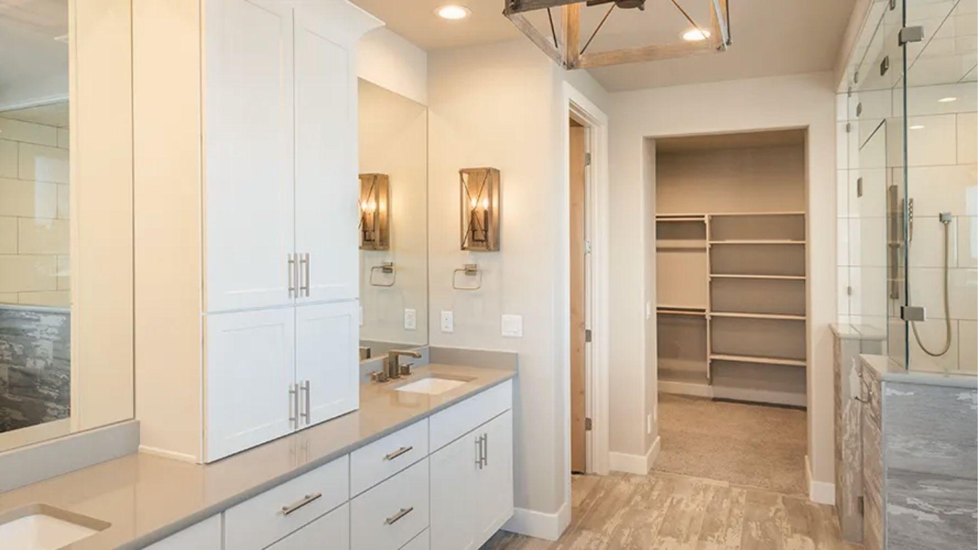 Transitional master bathroom with dual vanities, sconces, and walk-through closet entry.
