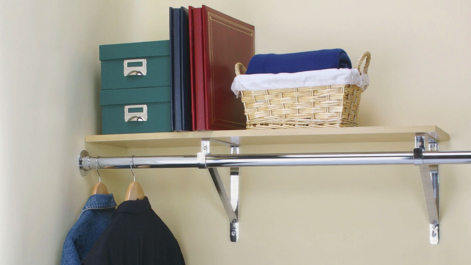 Chrome closet rod mounted under a wooden shelf with metal brackets, holding storage boxes and folded blankets above.