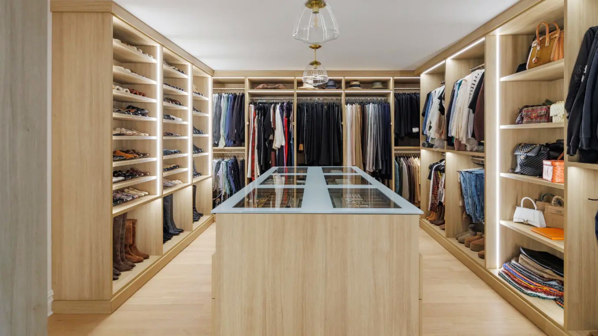 A grand luxury walk-in closet featuring rich wood tones, crystal chandelier, and a Hollywood-style vanity mirror.