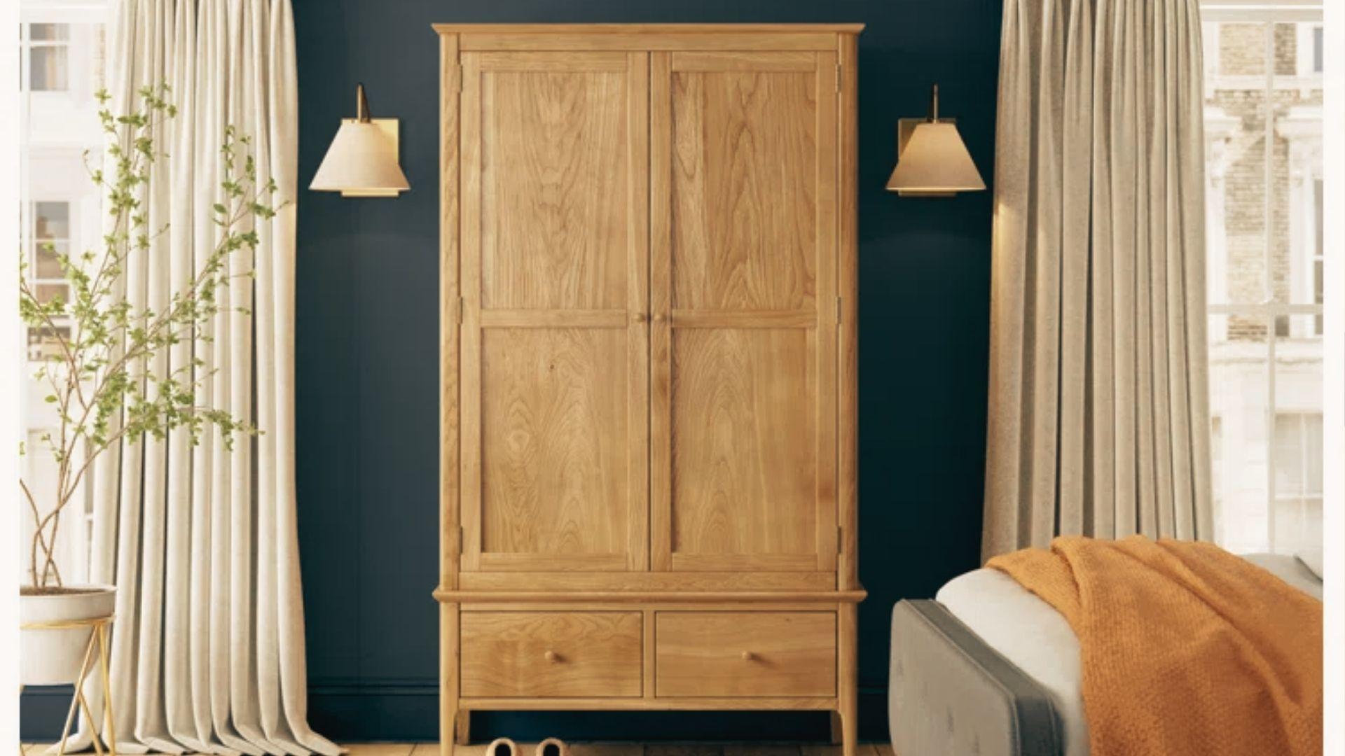 Classic natural oak double-door armoire with two bottom drawers in a bedroom with navy walls and cream curtains.