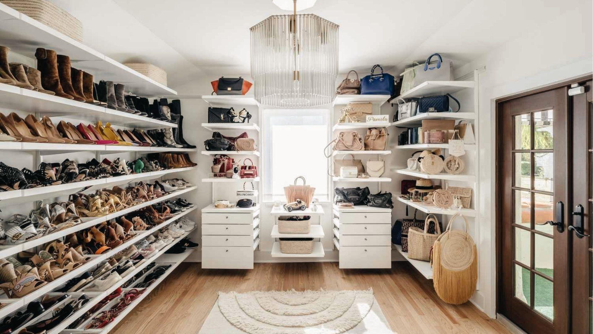 Sunlit shoe and bag closet with floor-to-ceiling shelves, chandelier, drawers, and glass doors.