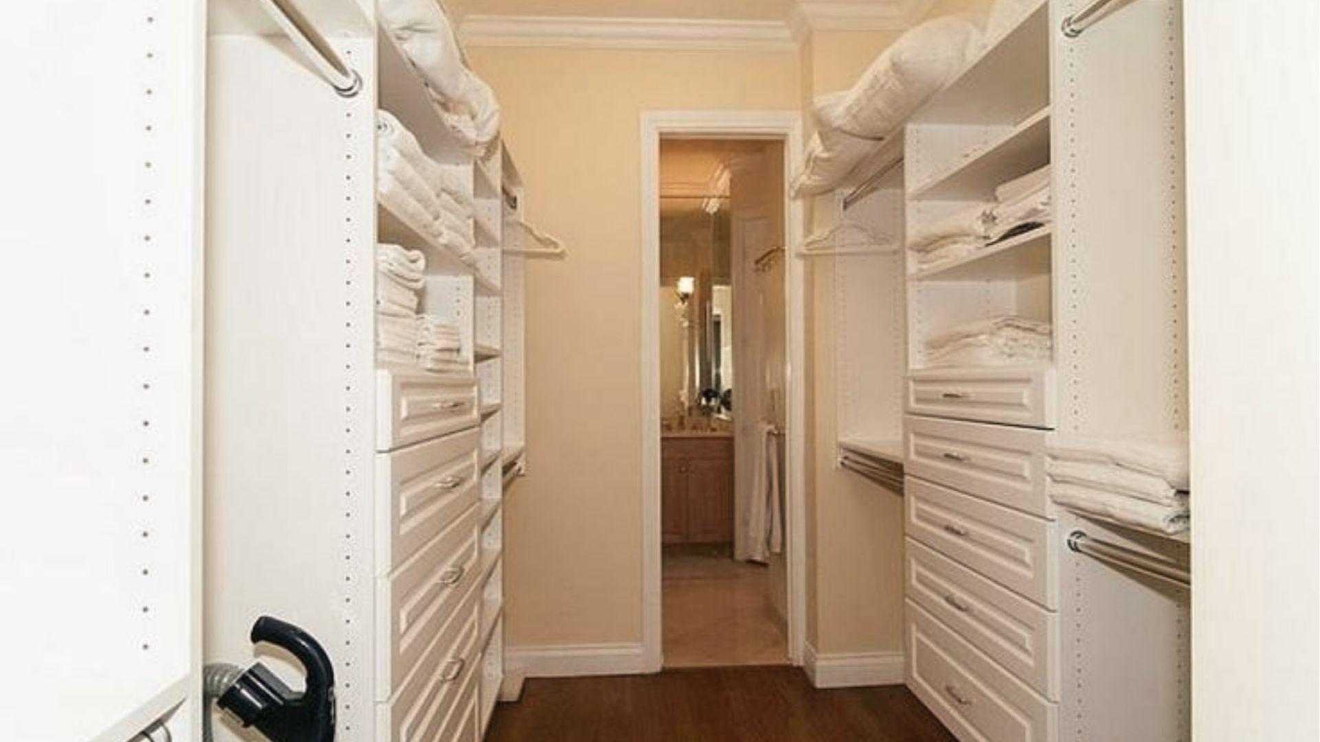 All-white walk-in closet layout with drawers, hanging rods, and direct master bathroom access.