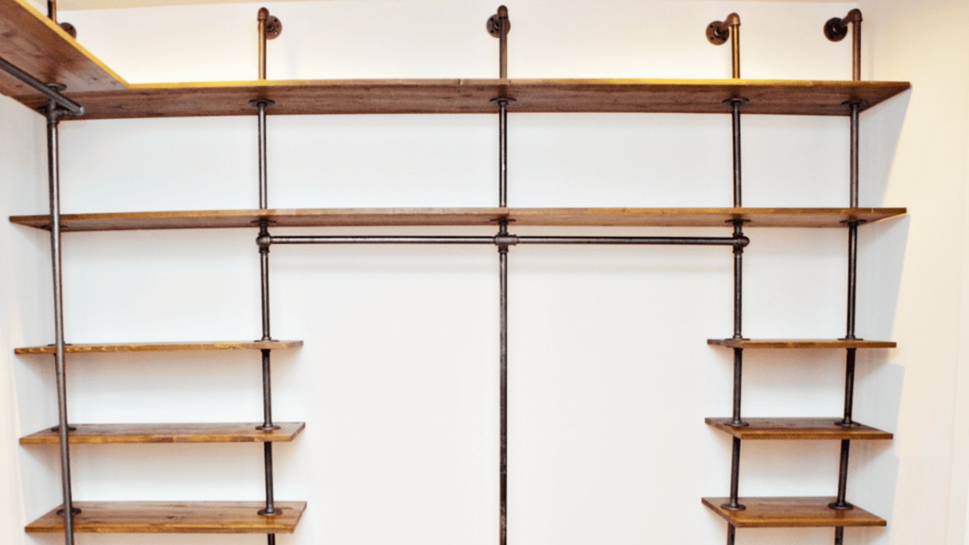 Industrial pipe wardrobe with wooden shelves, empty hanging rods, wall-mounted design, minimal.