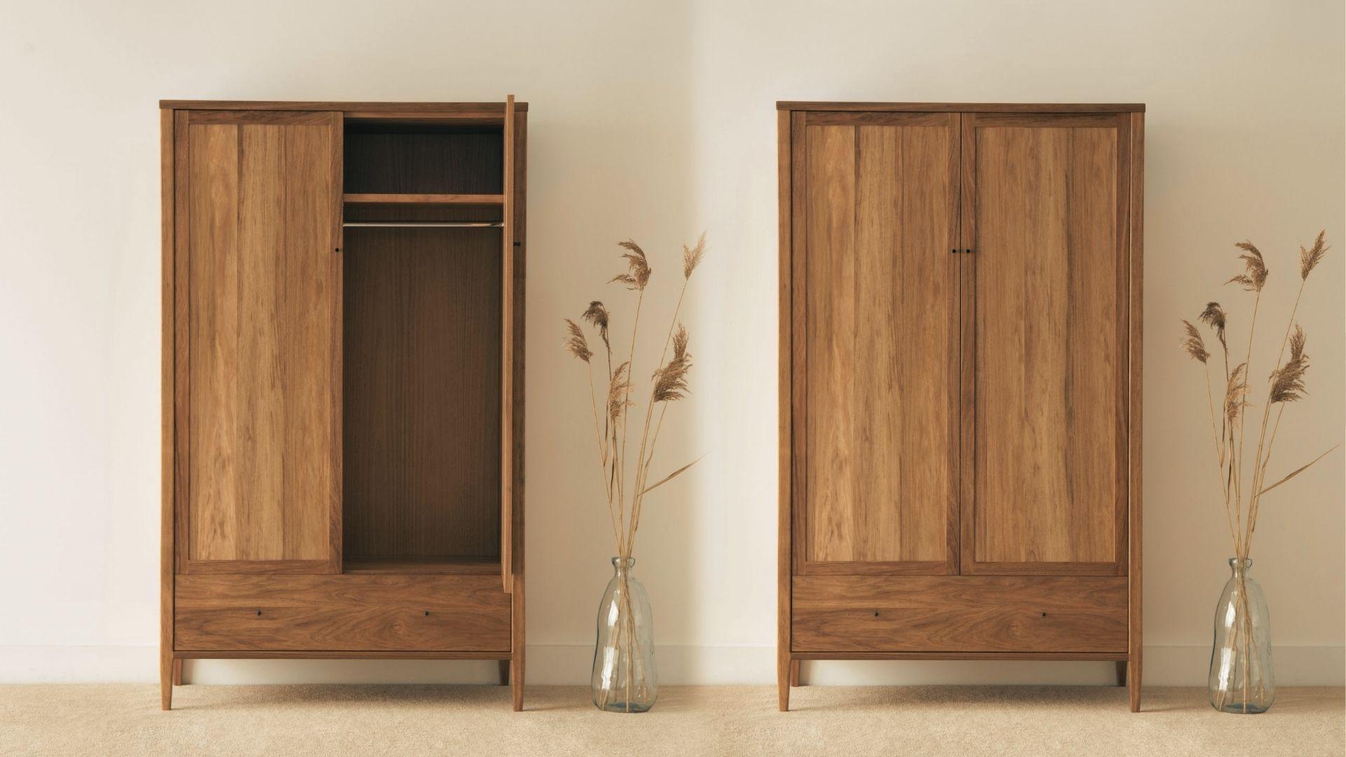 Minimalist freestanding wooden armoire set with two tall units against a beige wall and potted plants.
