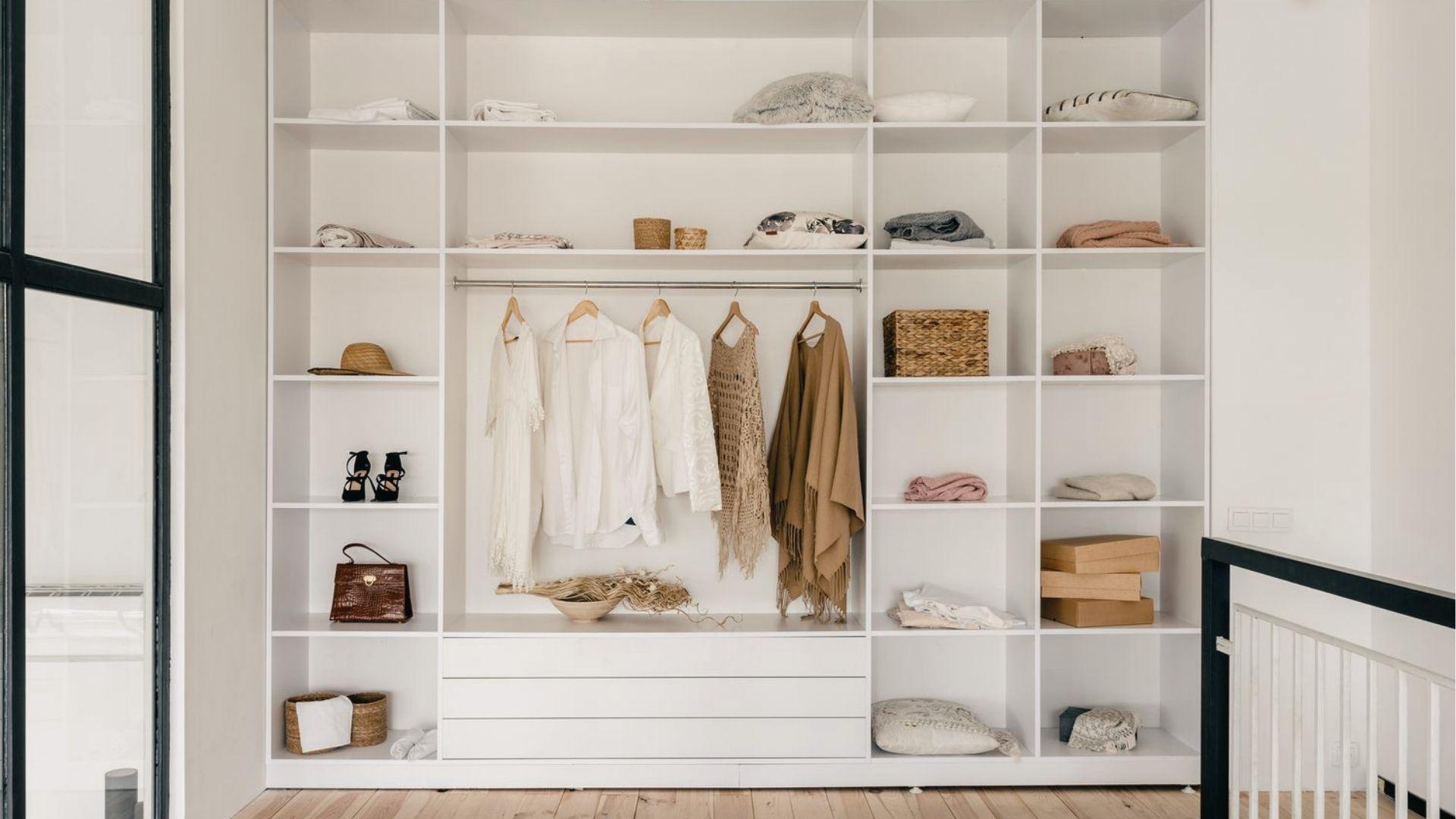 Minimalist white grid closet in bedroom with open shelves, hanging neutrals, baskets, and wood floors.