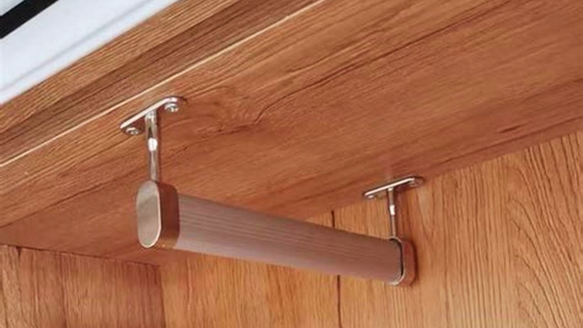 Close-up of a bronze closet rod mounted to a wooden shelf with two chrome end brackets.