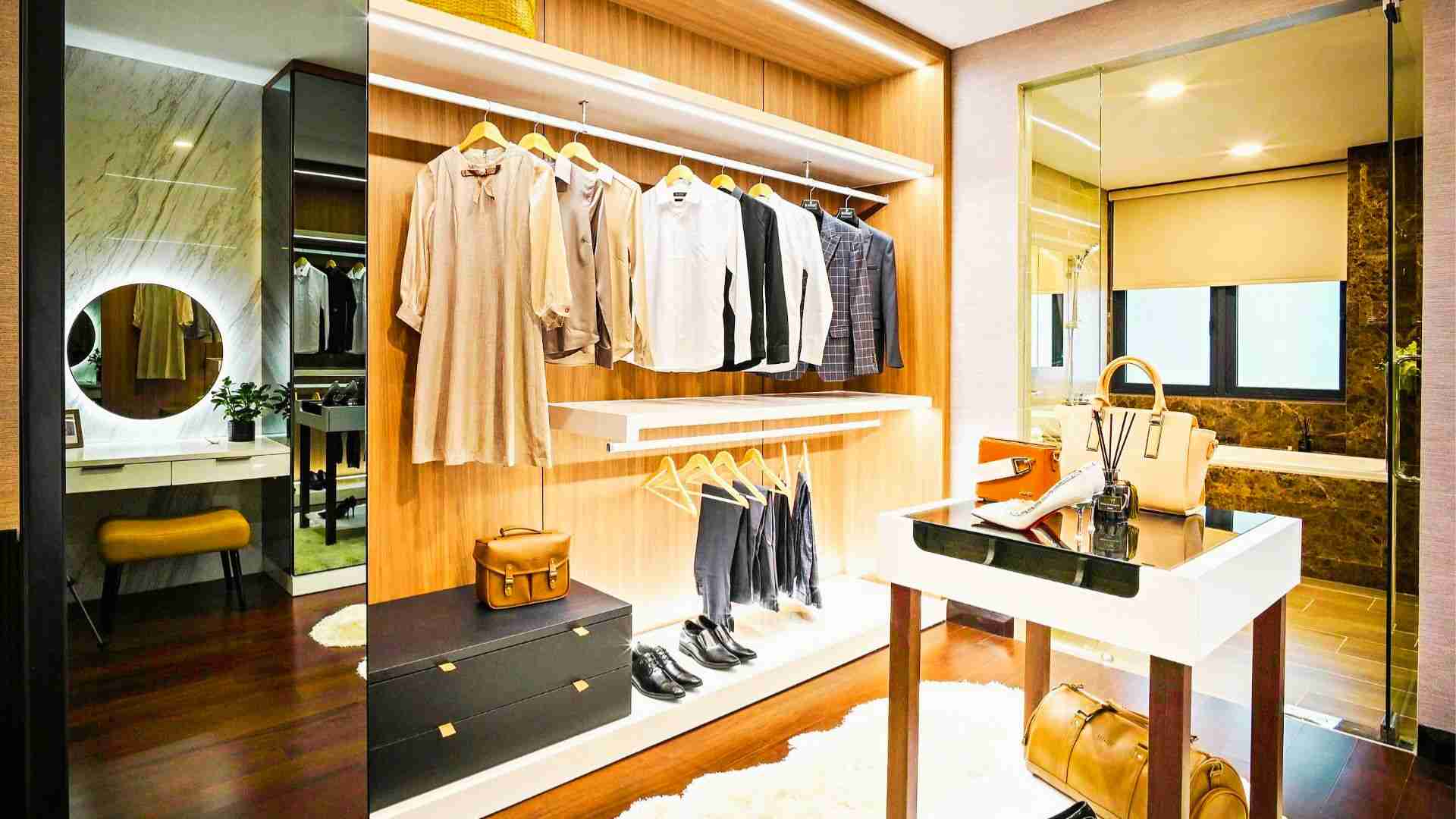 Luxury walk-in closet with wooden shelves, hanging clothes, vanity mirror, and designer handbags on display.