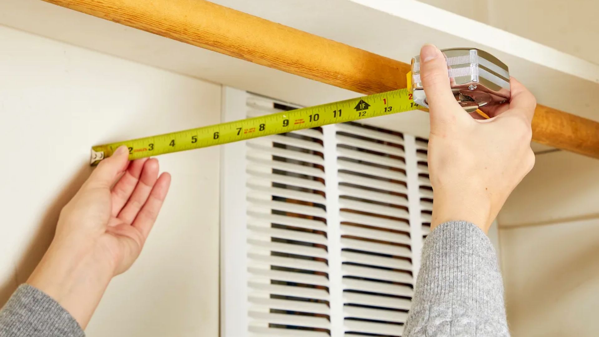 A person measuring the width of a closet space with a tape measure before installing a wooden closet rod.