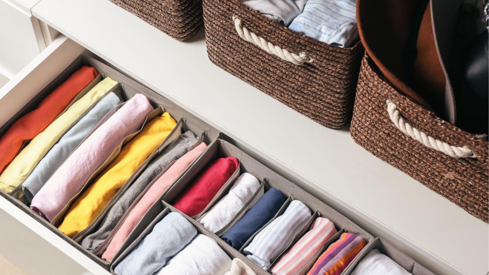 Drawer organizer with color-coded folded shirts in dividers and woven baskets for bedroom closet.
