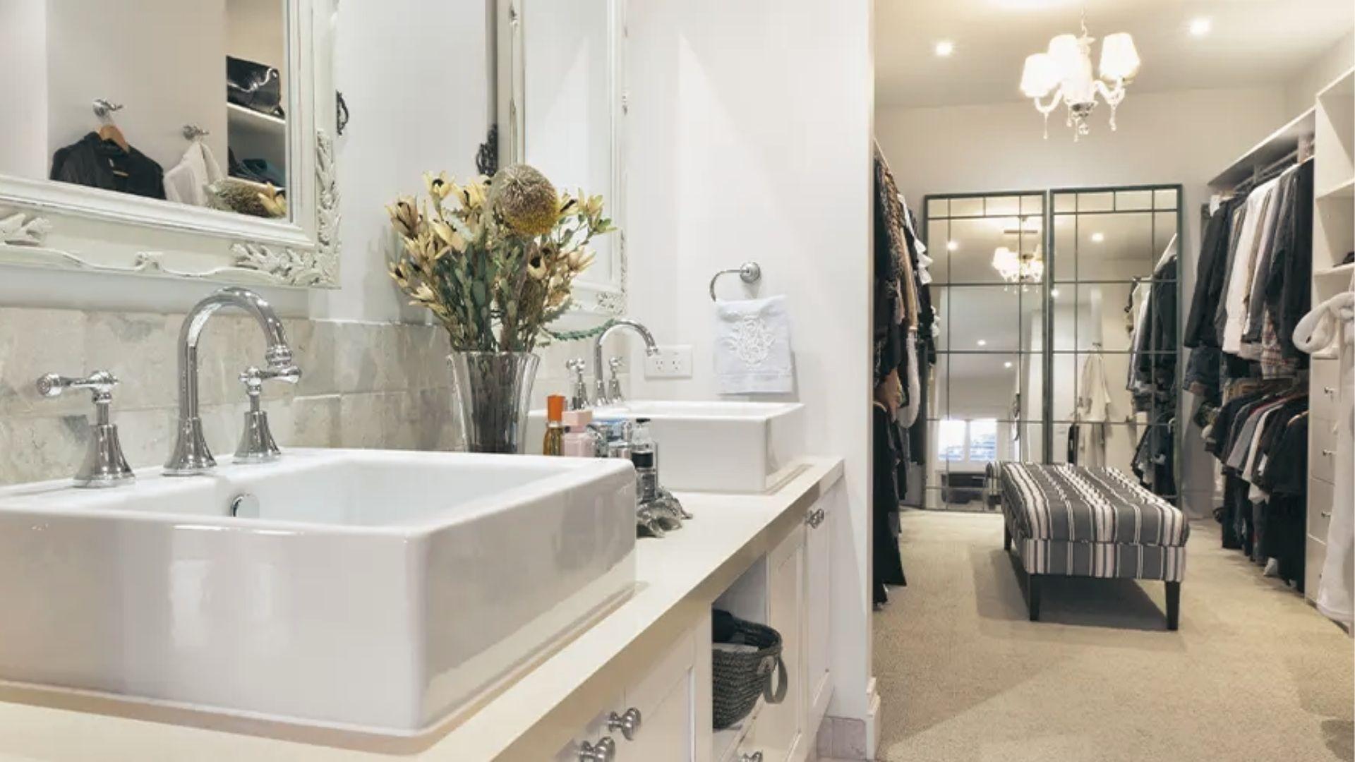 Farmhouse ensuite with dual vessel sinks opens into a carpeted walk-in closet with bench seat.