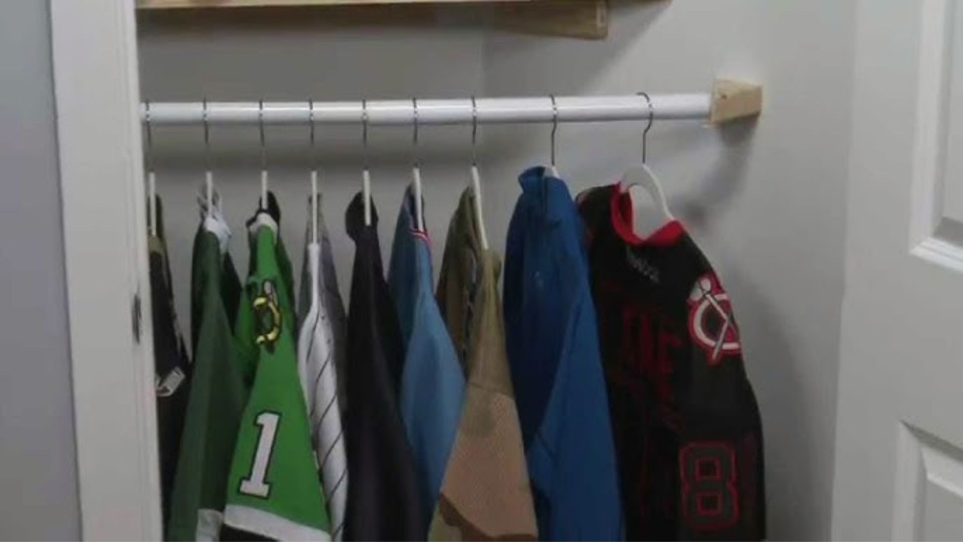 White closet rod installed between two walls with sports jerseys hanging on white plastic hangers.