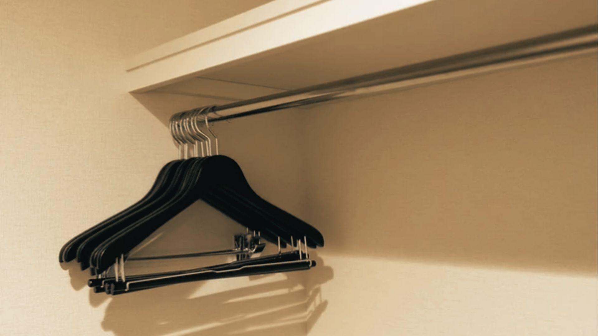 Black hangers on a metal rod with a shelf installed directly above, showing minimal clearance.