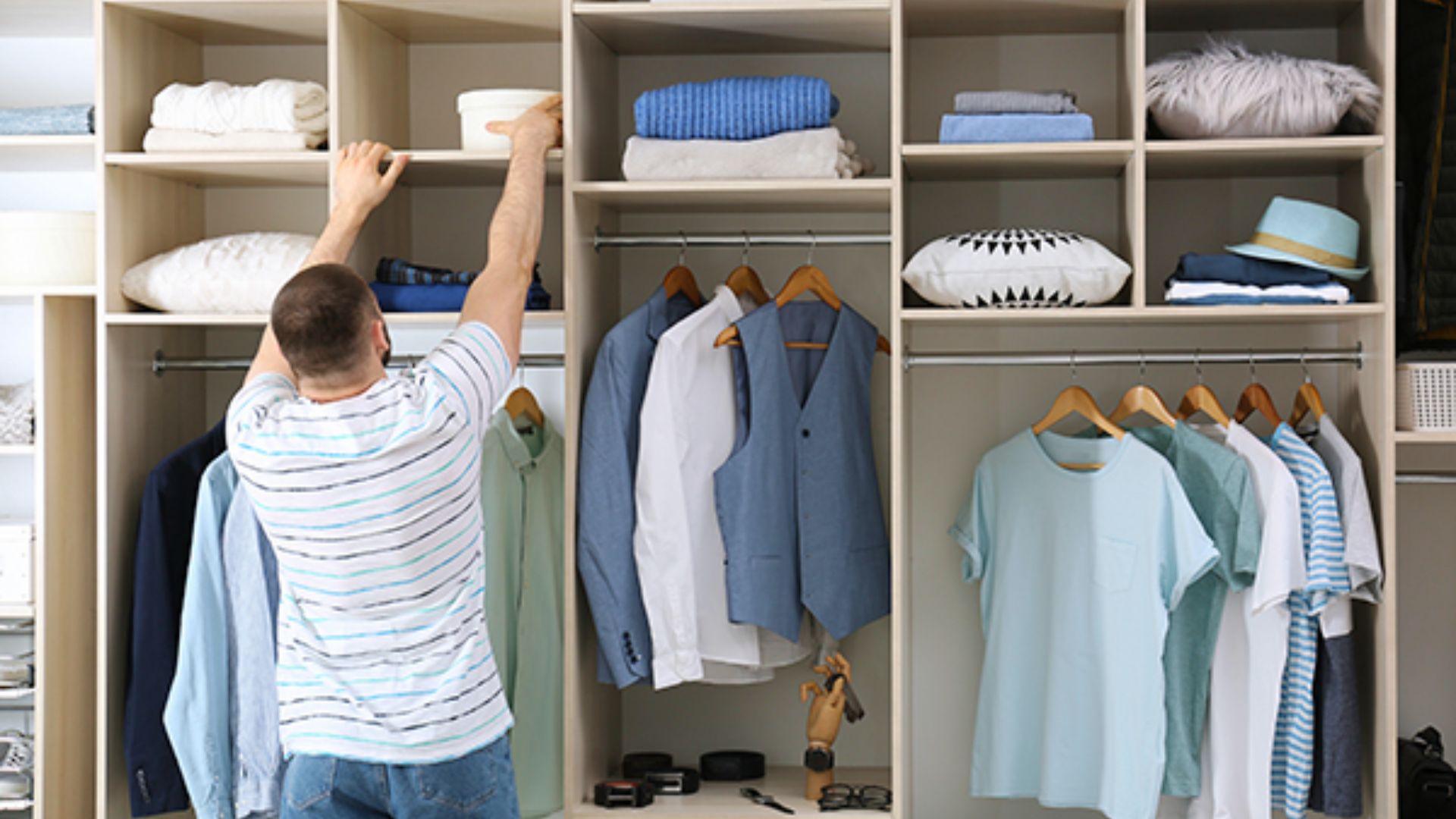 Man reaching to a high shelf in a closet with double hanging rods at standard heights.