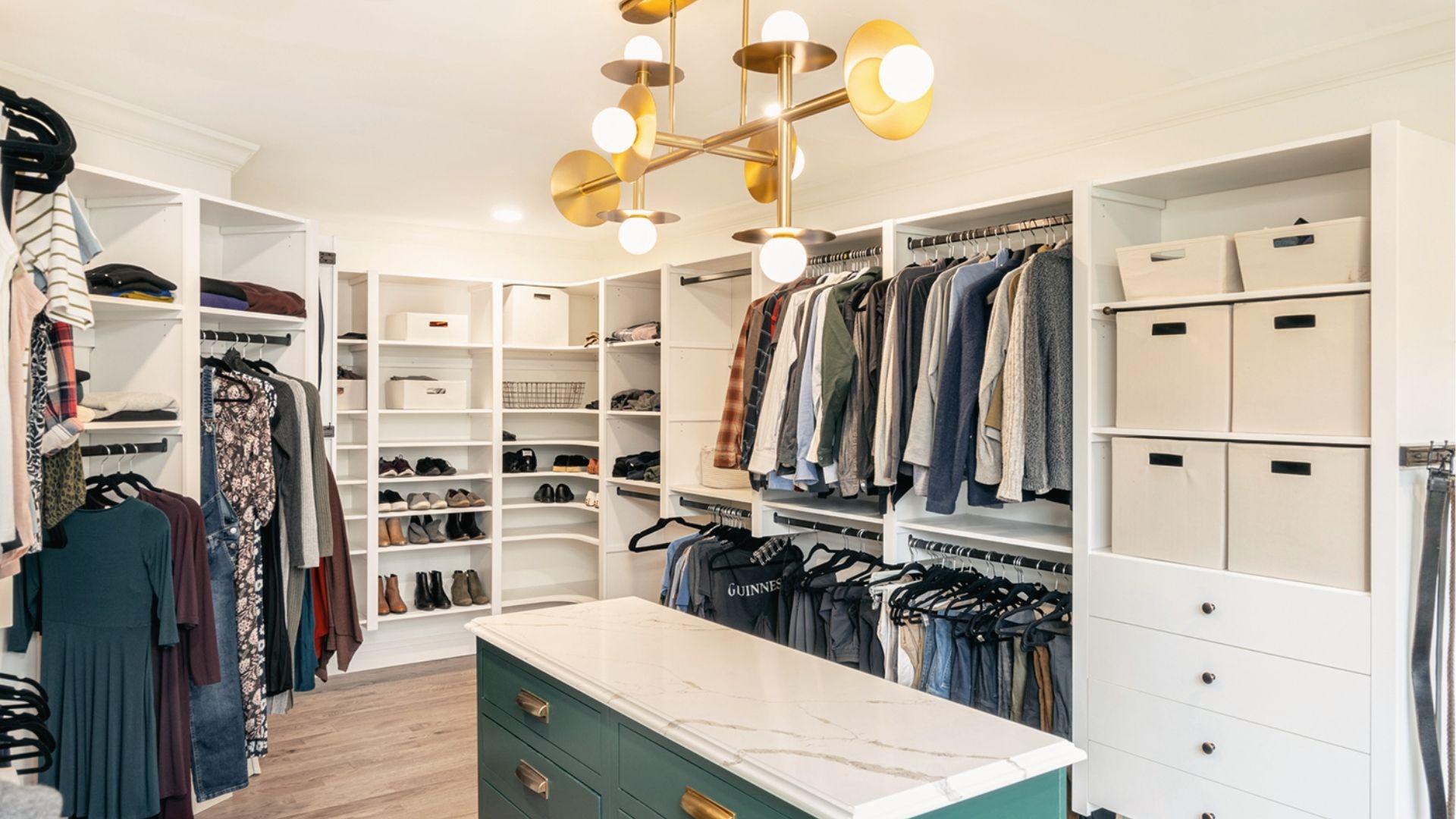 Large white walk-in closet with green island, gold chandelier, shoe shelves, and storage bins.